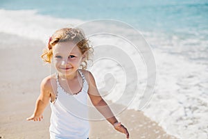 Adorable happy smiling little girl with curly hair on beach vacation