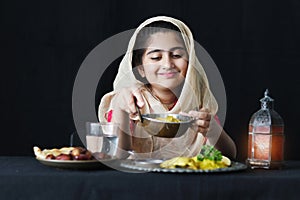Adorable happy smiling Muslim girl with beautiful eyes wearing traditional hijab, sitting at kitchen table, portrait of kid