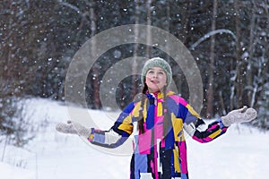 Adorable happy teenage girl is catching snowflakes with her hands in winter