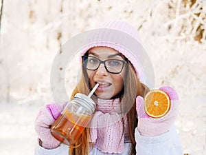 Adorable happy young blonde woman in pink knitted hat scarf having fun drinking hot tea from mug snowy winter park forest in natur