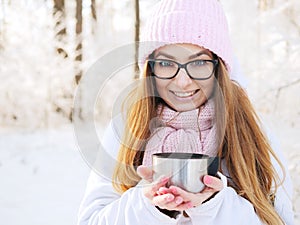 Adorable happy young blonde woman in pink knitted hat scarf having fun drinking hot tea from thermos cup snowy winter park forest