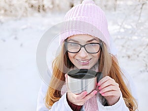 Adorable happy young blonde woman in pink knitted hat scarf having fun drinking hot tea from thermos cup snowy winter park forest