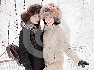 Adorable happy young brunette women holding hands in fur hat having fun snowy winter park forest in nature