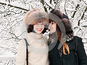 Adorable happy young brunette women girlfriends in fur hats having fun snowy winter park forest in nature