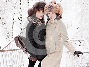 Adorable happy young brunette women holding hands in fur hat having fun snowy winter park forest in nature