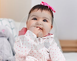 Adorable hispanic baby bitting fingers sitting on bed at bedroom
