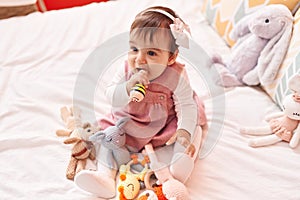 Adorable hispanic baby bitting maraca sitting on bed at bedroom