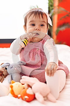 Adorable hispanic baby bitting maraca sitting on bed at bedroom