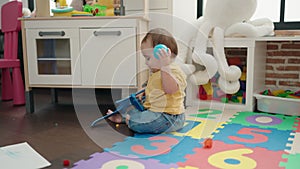 Adorable hispanic baby playing with ball and plane toy sitting on floor at kindergarten