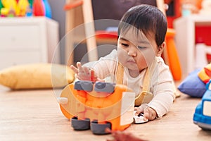 Adorable hispanic baby playing with cars toy lying on floor at kindergarten