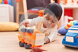 Adorable hispanic baby playing with cars toy lying on floor at kindergarten