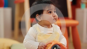 Adorable hispanic baby playing with cars toy sitting on floor at kindergarten