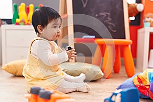 Adorable hispanic baby playing with cars toy sitting on floor at kindergarten