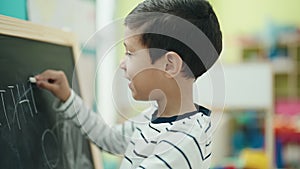 Adorable hispanic boy preschool student writing on blackboard at classroom