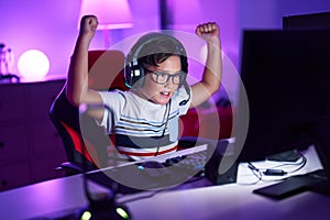 Adorable hispanic boy streamer playing video game with winner expression at gaming room