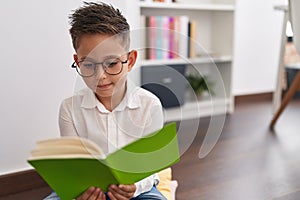 Adorable hispanic boy student smiling confident reading book at library school