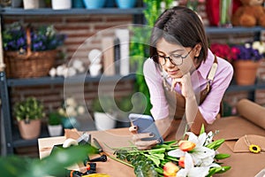 Adorable hispanic girl florist smiling confident using smartphone at flower shop