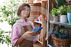 Adorable hispanic girl florist smiling confident using touchpad at flower shop