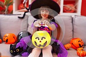 Adorable hispanic girl having halloween party holding pumpkin lamp basket at home