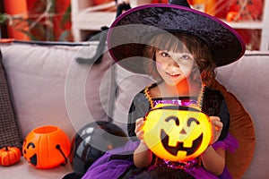 Adorable hispanic girl having halloween party holding pumpkin lamp basket at home