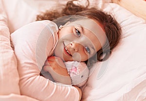 Adorable hispanic girl hugging rabbit doll lying on bed at bedroom