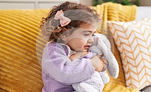 Adorable hispanic girl hugging rabbit toy sitting on sofa at home