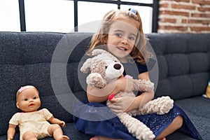 Adorable hispanic girl hugging rabbit toy sitting on sofa at home