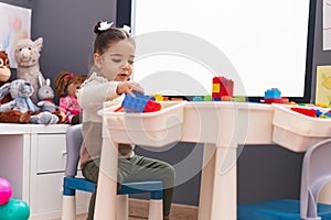 Adorable hispanic girl playing with construction blocks sitting on table at kindergarten