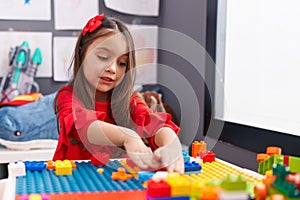 Adorable hispanic girl playing with construction blocks sitting on table at kindergarten