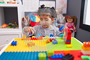 Adorable hispanic girl playing with construction blocks sitting on table at kindergarten