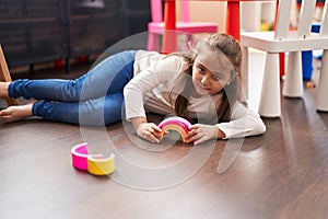 Adorable hispanic girl playing with toys lying on floor at kindergarten