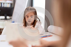 Adorable hispanic girl playing with toys sitting on table at classroom