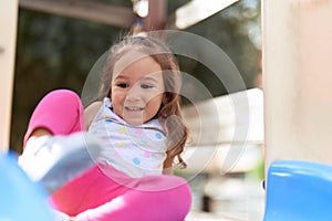Adorable hispanic girl sitting on slide playing at park playground