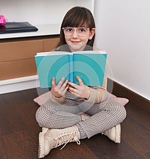 Adorable hispanic girl student smiling confident reading book at library school
