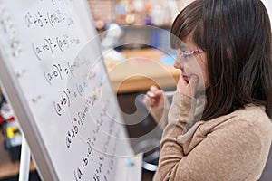 Adorable hispanic girl student standing by chalkboard solving maths exercise at classroom