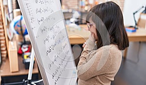 Adorable hispanic girl student standing by chalkboard solving maths exercise at classroom