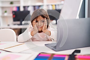 Adorable hispanic girl student using laptop with worried expression at classroom