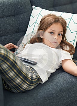 Adorable hispanic girl watching tv lying on sofa at home
