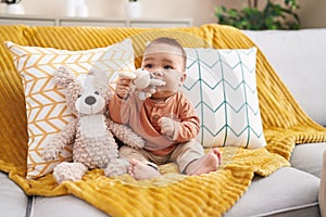 Adorable hispanic toddler bitting toy sitting on sofa at home