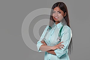 Adorable indian female doctor nurse with stethoscope in aquamarine dress on grey background