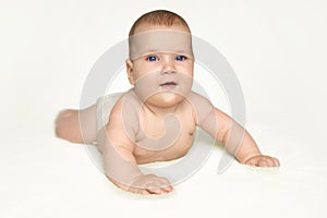Adorable infant baby boy with blue eyes laughs and crawls on bedding wearing diaper. White background photo