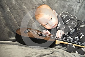 Adorable kid baby boy playing guitar and singing a song at home on gray couch