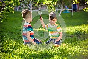 Adorable kid boy making fire on paper with a magnifying glass outdoors, on sunny day.