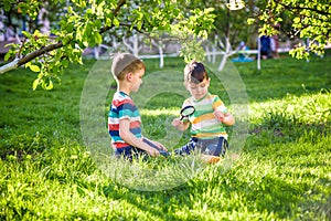 Adorable kid boy making fire on paper with a magnifying glass outdoors, on sunny day