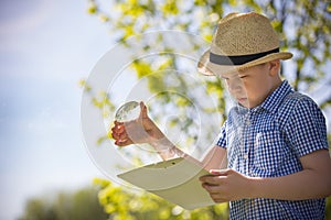 Adorable kid boy making fire on paper with a magnifying glass outdoors, on sunny day. Child exploring fire nature in the garden.