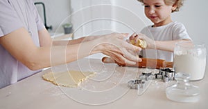 Adorable kid cooking pastry with mother holding dough smiling in kitchen
