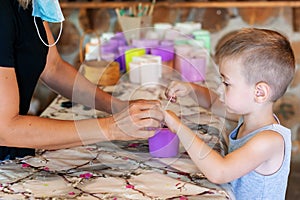 Adorable kid with craftsperson trimming candle wicks on homemade candles