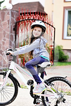 Adorable kid girl in blue helmet riding her bike