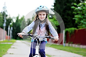 Adorable kid girl in blue helmet riding her bike