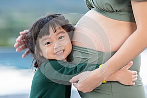 Adorable kid girl hugging pregnant mother belly to hearing sound of baby.Lovely little girl loving and waiting for newborn sister